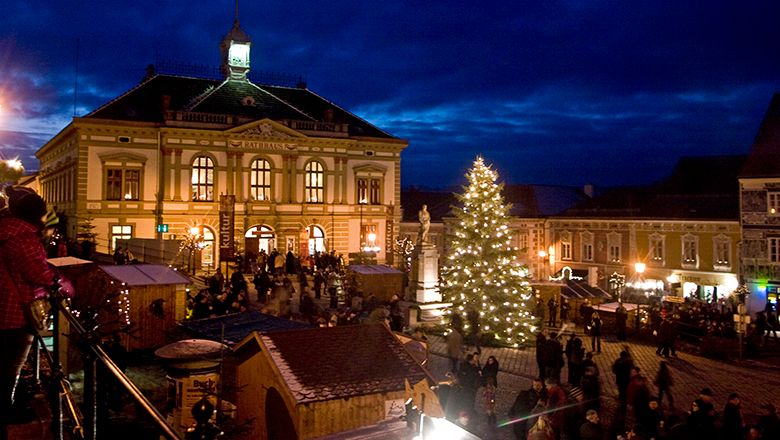Weihnachtsmarkt bei Nacht mit beleuchtetem Weihnachtsbaum und historischem Rathausgebäude im Hintergrund