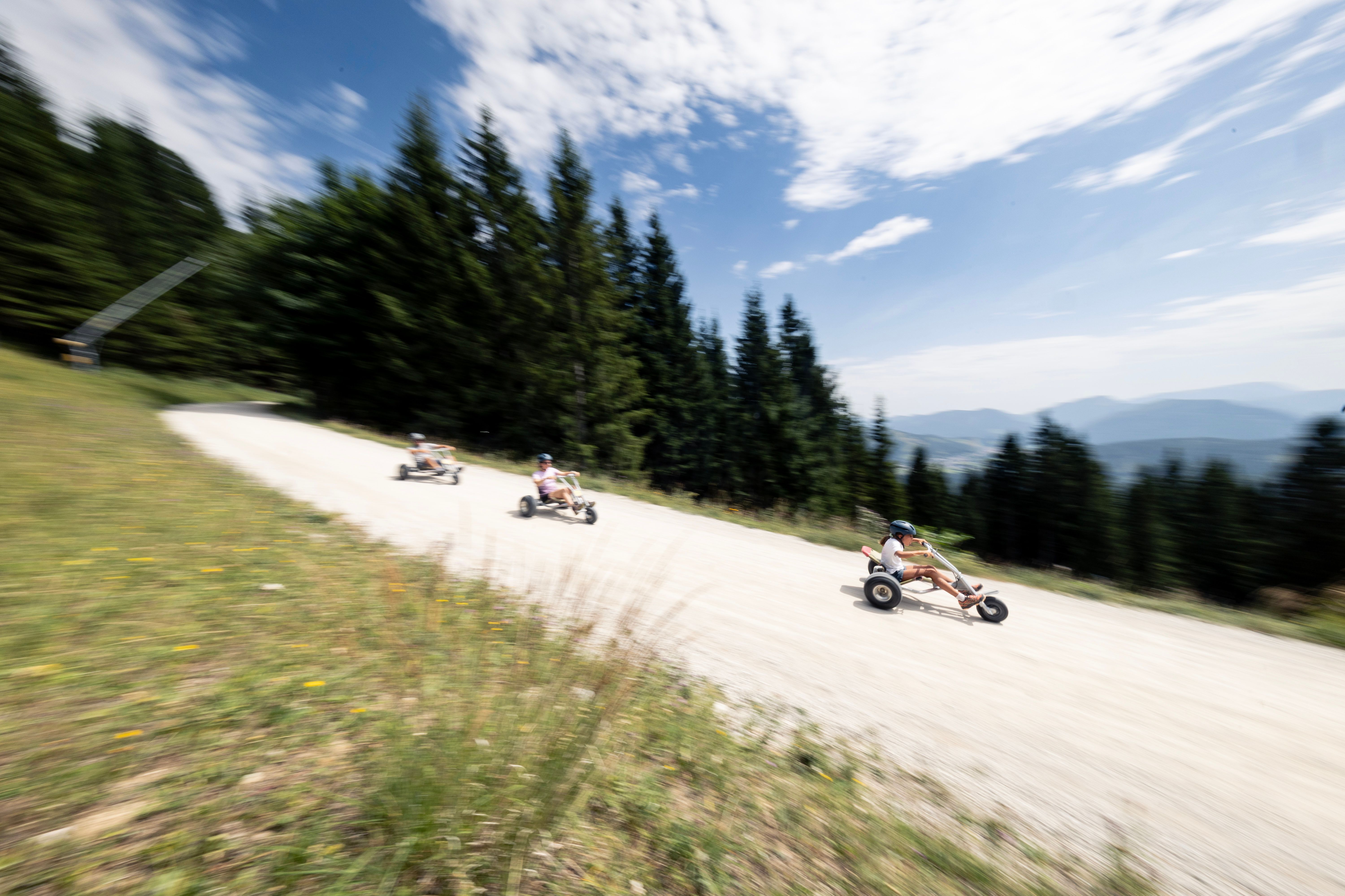 Drei Personen fahren mit Helmen in Mountaincarts eine kurvige Schotterstraße auf der Gemeindealpe hinunter.