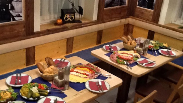 Ein gedeckter Tisch in einem rustikalen Restaurant mit Brot, Aufschnitt und Salaten.