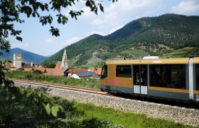 Der goldene Triebwagen der Wachaubahn fährt an einer Ortschaft vorbei