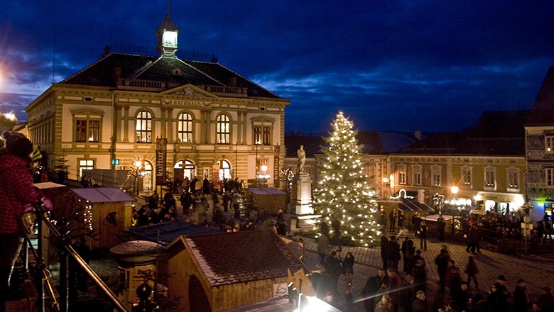 Weihnachtsmarkt bei Nacht mit beleuchtetem Weihnachtsbaum und historischem Rathausgeb&auml;ude im Hintergrund