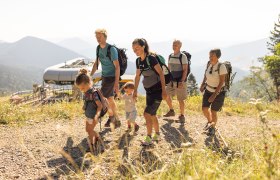 Famlilie bestehend aus 2 kleinen Kindern, Eltern und Großeltern wandert oberhalb der Sesselbahn.