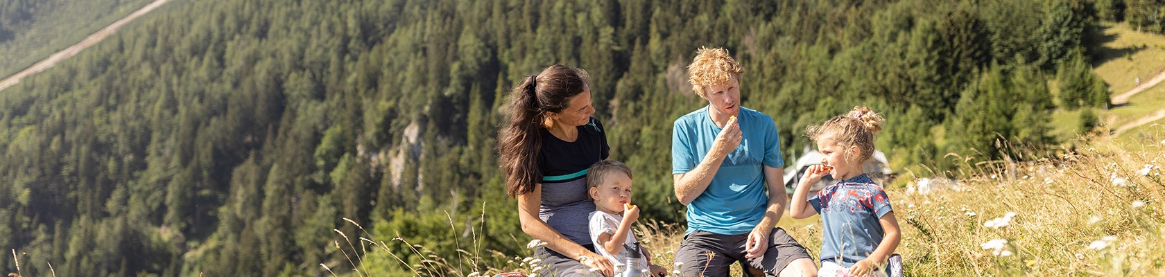 Familie sitzt auf blühender Wiese mit Picknickdecke und Snacks